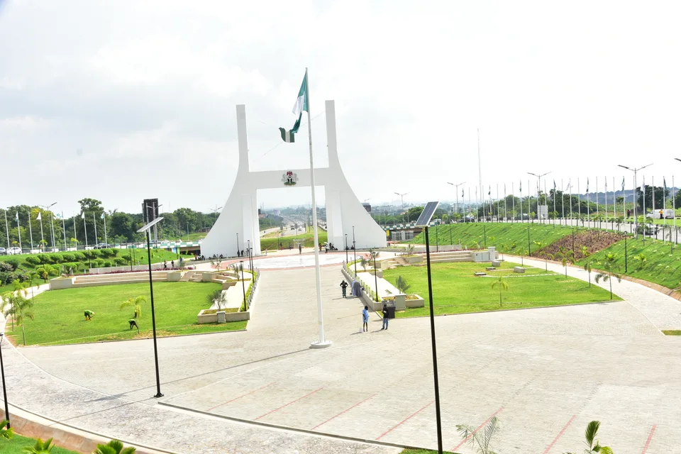 Abuja City Gate with the Nigerian flag, landscaped public grounds and roads beyond